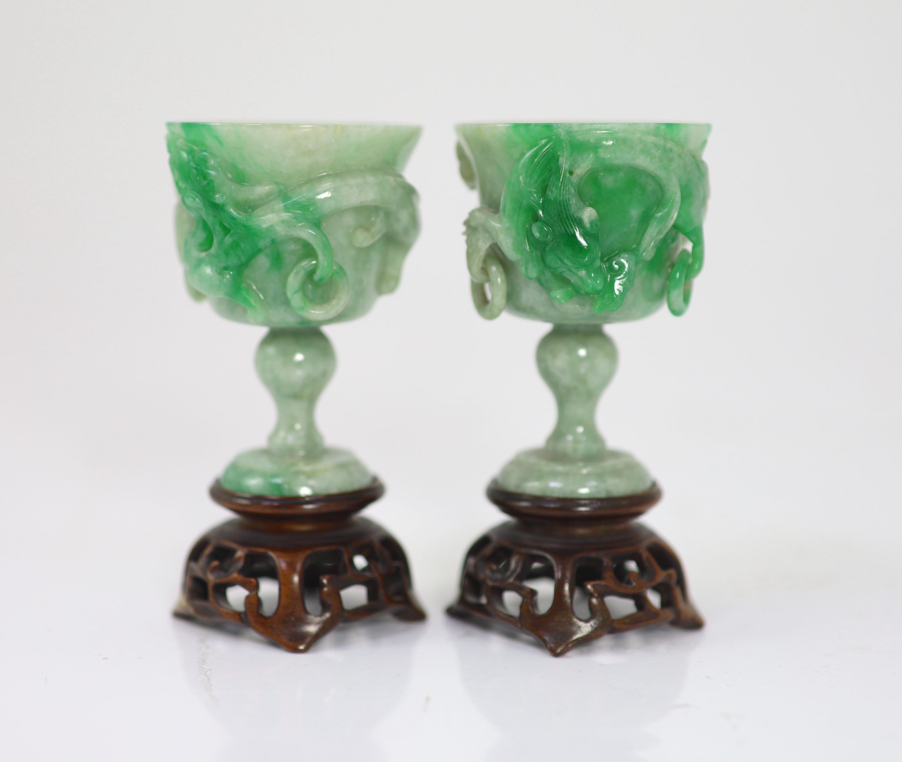 A pair of Chinese small jadeite stem cups, 20th century, 7.2cm high, carved wood stands